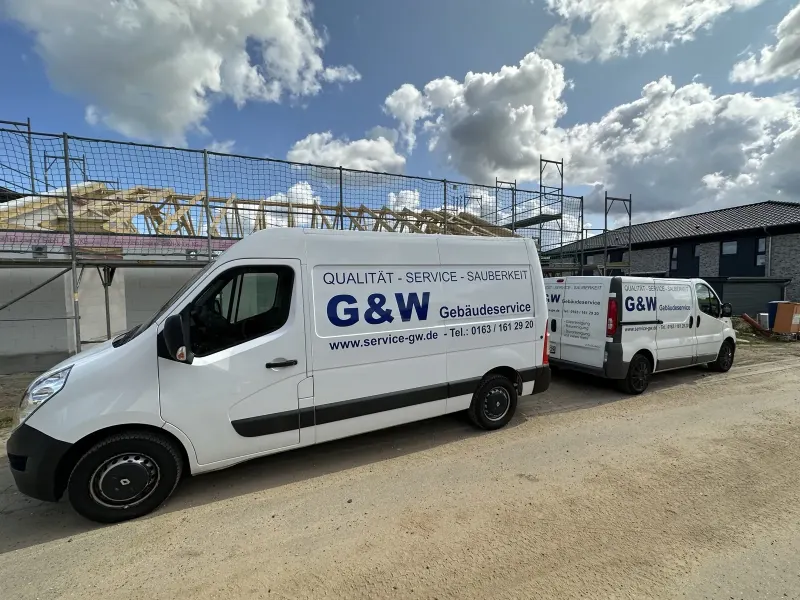 Zwei weiße G&W-Transporter vor einem Neubau mit Gerüst.