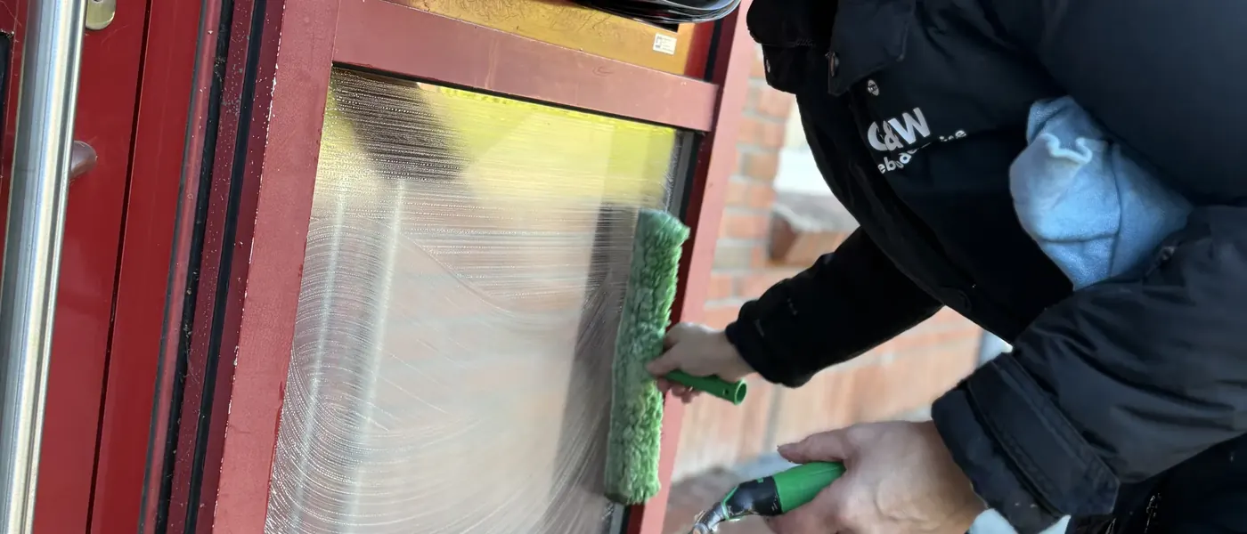 Eine Mitarbeiterin von G&W wäscht die Glasscheibe einer roten Eingangstür mit dem Einwascher ein.